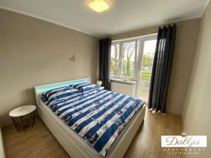 a bedroom with a bed with a blue comforter and a window at W Dablju - Apartementy nad morzem in Władysławowo