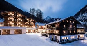 un grand bâtiment dans la neige avec des lumières allumées dans l'établissement Hotel Oberraindlhof, à Senales