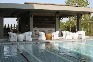 a pool with white chairs next to a house at Navela Hotel & Convention in Ratchaburi