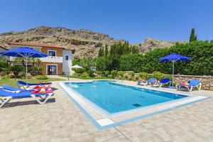 una piscina con sedie e ombrelloni accanto a una casa di Villa Clive by Villa Plus a Líndos