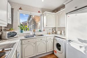 cocina con armarios blancos, fregadero y nevera en 2-Bed spacious Flat-2-minute walk to tube station, en East Barnet 9 fotos más