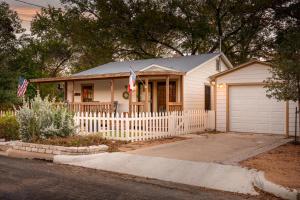 a small white house with a fence and an american flag at LeMay Haus - Fire Pit, Heated Pool & Close to Main in Fredericksburg