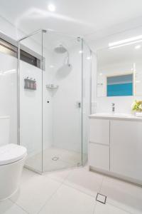 a white bathroom with a shower and a toilet at Byron Bayside Central Studio Apartments in Byron Bay