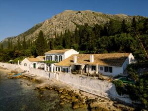 a house by the water with a mountain in the background at Nissaki Olive Press Villas in Nisakion