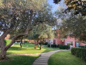 a walkway in front of a pink building with trees at Cala Rosa Club Hotel in Stintino