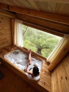 a woman laying in a hot tub in a tree house at Chalés Recanto do Vale - GRALHA AZUL in Bom Jardim da Serra
