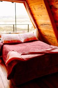 a bed in a log cabin with a window at Chalés Recanto do Vale - GRALHA AZUL in Bom Jardim da Serra