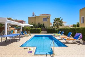 a swimming pool with chairs and a table and a house at Villa Azalea by Villa Plus in Peyia
