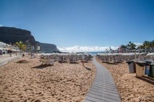a sandy beach with chairs and umbrellas and the ocean at Apartamento Los Angeles 2 in Puerto de Mogán