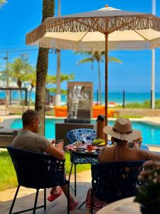 two people sitting at a table under an umbrella near a pool at Luna Hotel Boutique - Frente à Praia in Guarujá