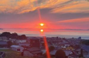 einen Sonnenuntergang über einer Stadt mit der Sonne am Himmel in der Unterkunft Shikochu Base - Vacation STAY 76591v in Shikokuchuo