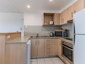 une cuisine avec des armoires en bois et un réfrigérateur blanc dans l'établissement The Pool Resort Kingscliff - 2BR Dual Key and 1BR (7303/7304) - Holiday Management Co., à Kingscliff