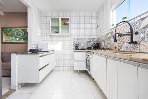 a white tiled kitchen with white cabinets and a sink at Refúgio Tropical Casa de Praia com Piscina Climatizada e 4 Suítes e garagem 3 carros, 800 mtrs da praia internet 700 mbps, condomínio privado com pista de skate , quadra de futevôlei , campos e quadras de futebol! in Cabo Frio