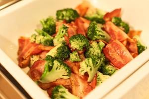 a white plate of food with broccoli and bacon at Hotel Paco Obihiro Chuo in Obihiro
