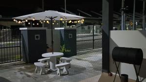 a table and benches with an umbrella in front of a fence at Santai Homestay PD in Port Dickson