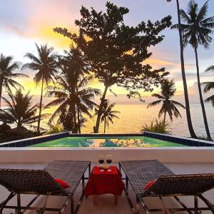 a pool with two chairs and a table with wine glasses at ArtVilla Camiguin - Luxus Homestay mit Infinity Pool und Sunset View in Mambajao