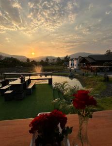 a vase of flowers sitting on a table with a sunset at ม่วนใจ๋ปันสุข โฮมสเตย์แอนคาเฟ่ Muanjai punsuk homestay and cafe in Chom Thong