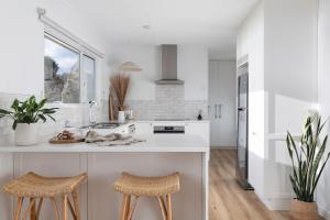 a white kitchen with two stools and a sink at The Red Door Strahan in Strahan