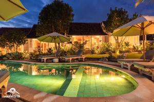a swimming pool with chairs and umbrellas in front of a house at D'Pendem Cottage's by Bukit Vista in Uluwatu