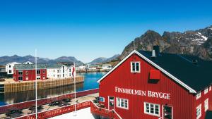 a red building next to a body of water with mountains at Finnholmen Brygge in Henningsvær