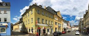 a yellow building on a city street with cars parked at Pension & Ferienwohnungen Töpferstüb'l in Saalfeld