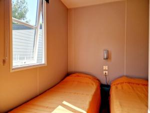 zwei Betten in einem kleinen Zimmer mit Fenster in der Unterkunft Camping Del Mar 52, Mobile Home Excellence, 3 chambres, 6 personnes, bord de mer in Argelès-sur-Mer + 7 Fotos