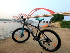 a bike parked on the beach with a bridge in the background at Emma Homestay in Pattiyūrgrāmam