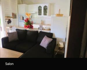 a living room with a black couch and a kitchen at Villa Ti Gîte - Piscine privée in Le Marin