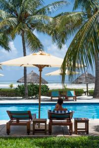 a man sitting in a chair under an umbrella next to a swimming pool at Kisiwa on the Beach in Paje