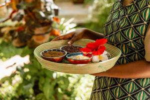 a woman holding a plate with three bowls of food at Kisiwa on the Beach in Paje