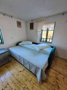 a bedroom with a bed with blue sheets and two windows at Căsuță Baciului in Berevoeşti