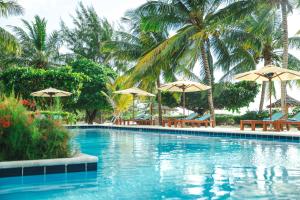 a swimming pool with chairs and umbrellas and palm trees at Kisiwa on the Beach in Paje