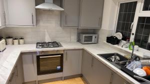 cocina con armarios blancos, fogones y fregadero en Raeburn Avenue House, en Worcester Park