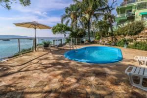 a swimming pool with chairs and an umbrella next to the water at Pousada Praia da Lagoinha in Bombinhas
