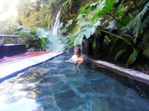 Ein Mann im Schwimmbad vor einem Wasserfall. in der Unterkunft Cabañas y Casas Hualles in Coñaripe