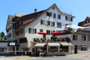 un gran edificio blanco con sombrillas rojas en una calle en B&B Caffètino-Vino en Richterswil