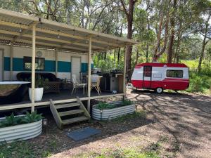Un camper parcheggiato sotto un tendone vicino a una casa. di Alice & Elvis, Crescent Head, Retro Caravans with Deck, Bathroom & Outdoor Bath in a Bush Setting near the Beach a Crescent Head