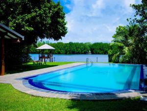a large blue swimming pool next to a lake at Okvin River Villa in Bentota