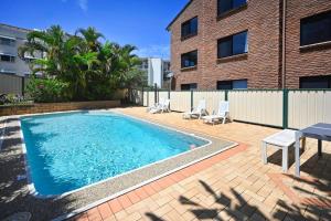 a swimming pool with chairs and a table and a building at Coastal Comfort, Relaxing Kings Beach Retreat in Caloundra
