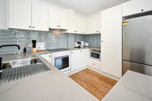 a kitchen with white cabinets and a stainless steel refrigerator at Coastal Comfort, Relaxing Kings Beach Retreat in Caloundra