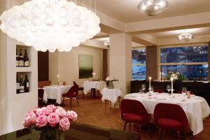 ein Restaurant mit weißen Tischen, rosa Blumen und einem Kronleuchter in der Unterkunft Bellevue Parkhotel & Spa - Relais & Châteaux in Adelboden