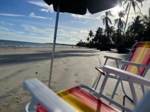 a beach with chairs and an umbrella and the ocean at Casa com piscina pertinho da Praia l Milagres Hospedagens in Pôrto de Pedras