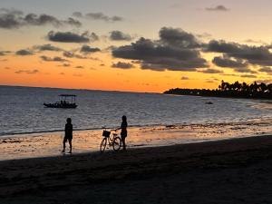 two people walking a bike on the beach at sunset at Casa com piscina pertinho da Praia l Milagres Hospedagens in Pôrto de Pedras