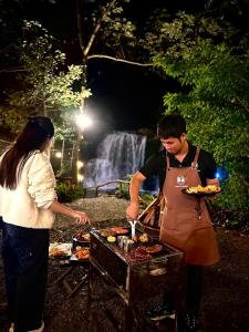 a man and a woman preparing food on a grill at Zenda Glamping in Bao Loc