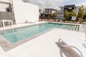 una piscina con 2 sillas blancas junto a un edificio en C & C By The Sea, en Coolum Beach