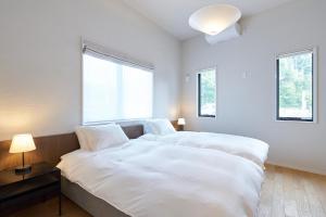 a white bedroom with two beds and two windows at Hayama Ocean Villa - 南葉山 オーシャンヴィラ - in Yokosuka