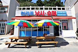 two picnic tables with umbrellas in front of a store at Taean Cheollipo Condon Pension in Taean