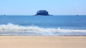 a wave on the beach with an island in the ocean at Taean The sea side Pension in Tohwang-ni +15 photos