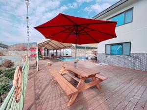 a wooden picnic table with a red umbrella on a deck at Cheongdo dolgorae poolhouse pension in Cheongdo