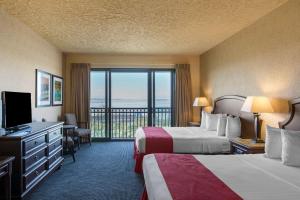 マスキーゴンにあるShoreline Inn & Conference Center, an Ascend Collection Hotelのベッド2台とバルコニー付きのホテルの部屋
